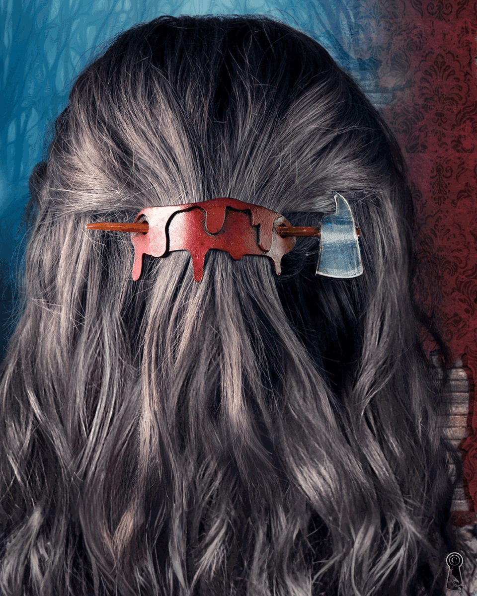 A person with dark hair and a blood and axe shaped hair clip in their hair against a textured wall.