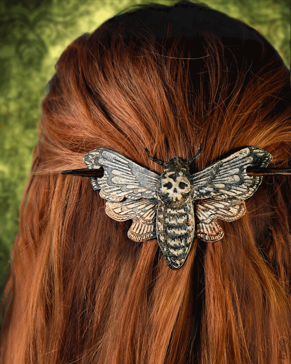 Hair slide shaped like a moth with skull design with a dark stick on red hair against a green background