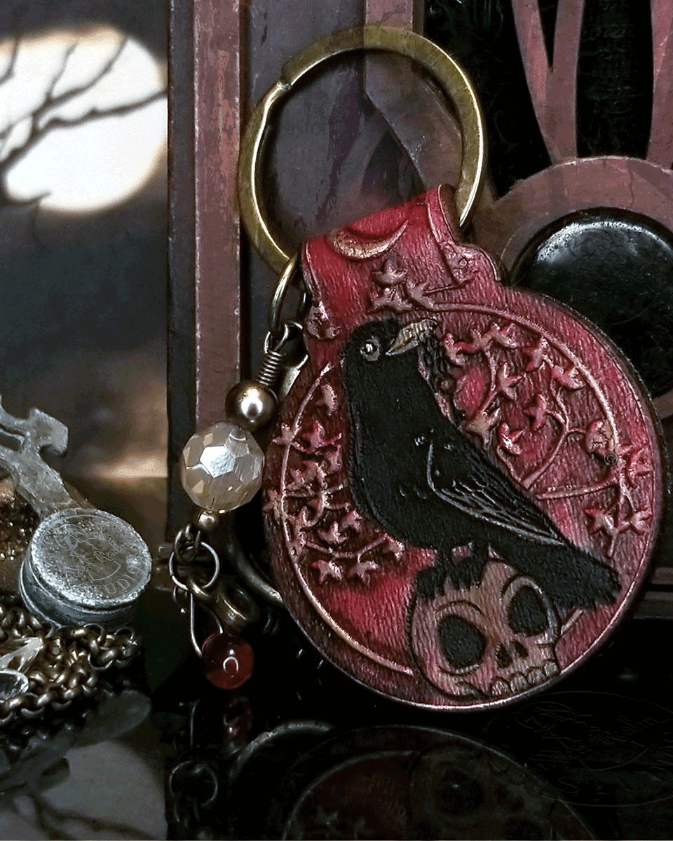 Decorative keychain with crow and skull design on a dark background