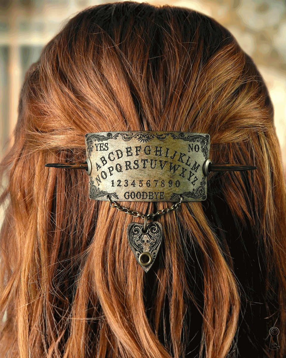 Hair accessory with Ouija board design and planchette charm on a person with long hair.