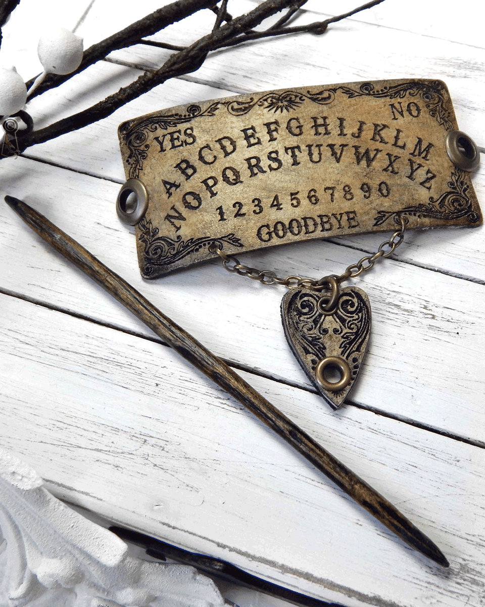 Ouija board slide with a dark wood stick and a planchette pendant on a white wooden surface.