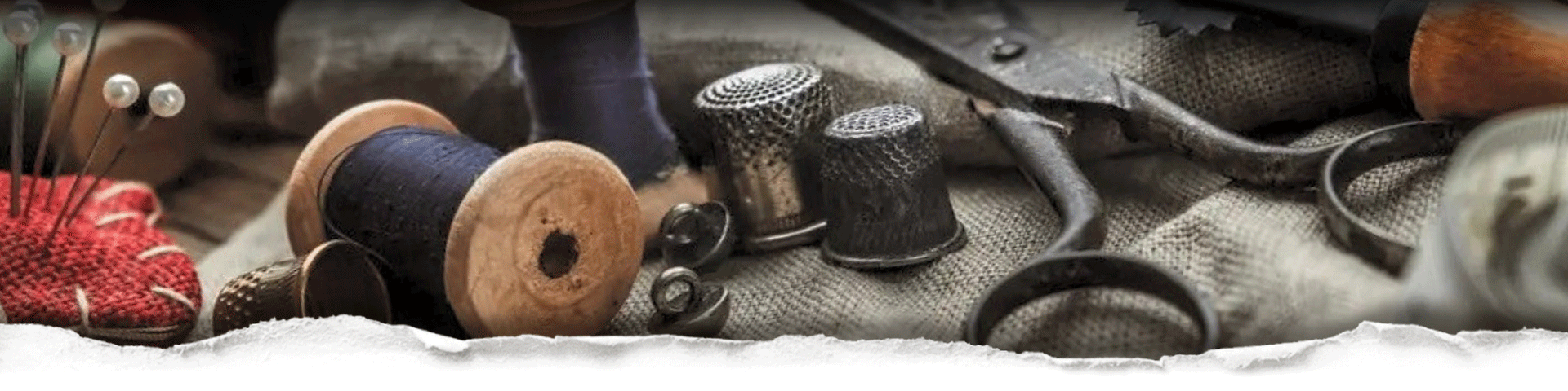 Vintage sewing tools including spools of thread, a thimble, and scissors on a textured fabric background behind torn paper
