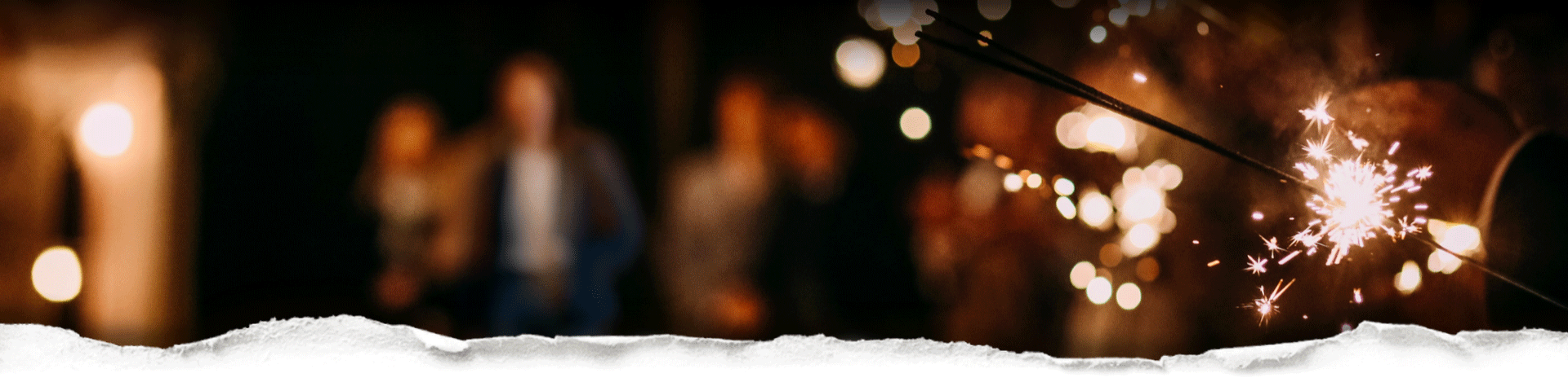 A gathering atmosphere with a close up on sparklers with blurred people in the background behind torn paper