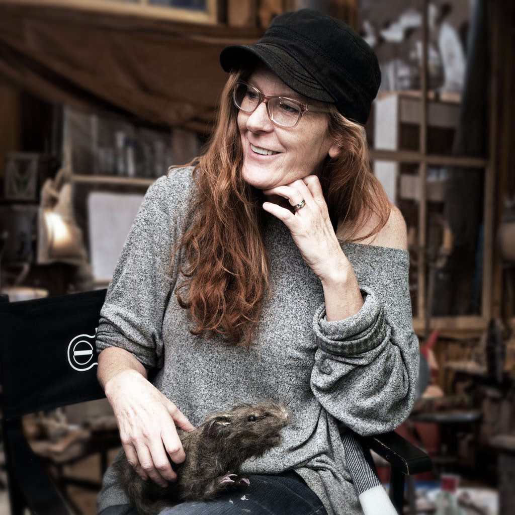 Gabby sitting in a mua chair holding a stuffed rat in a set dec room