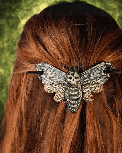 Hair slide shaped like a moth with skull design with a dark stick  on red hair against a green background 