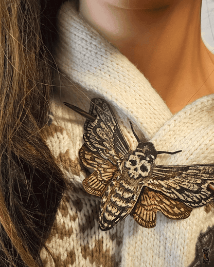 Close-up of a person wearing a white sweater with a large moth brooch.