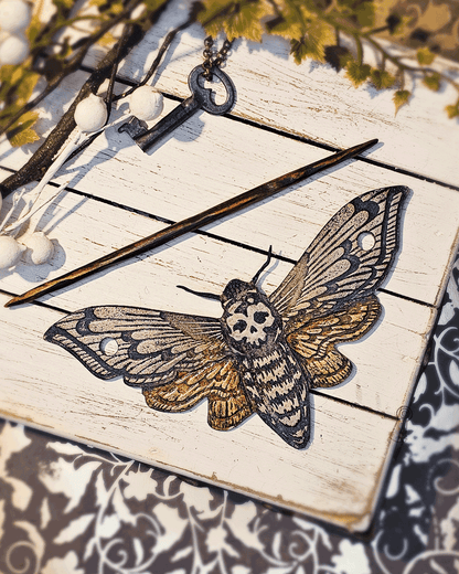 Decorative moth with skull design on a white wooden surface a dark wood stick.