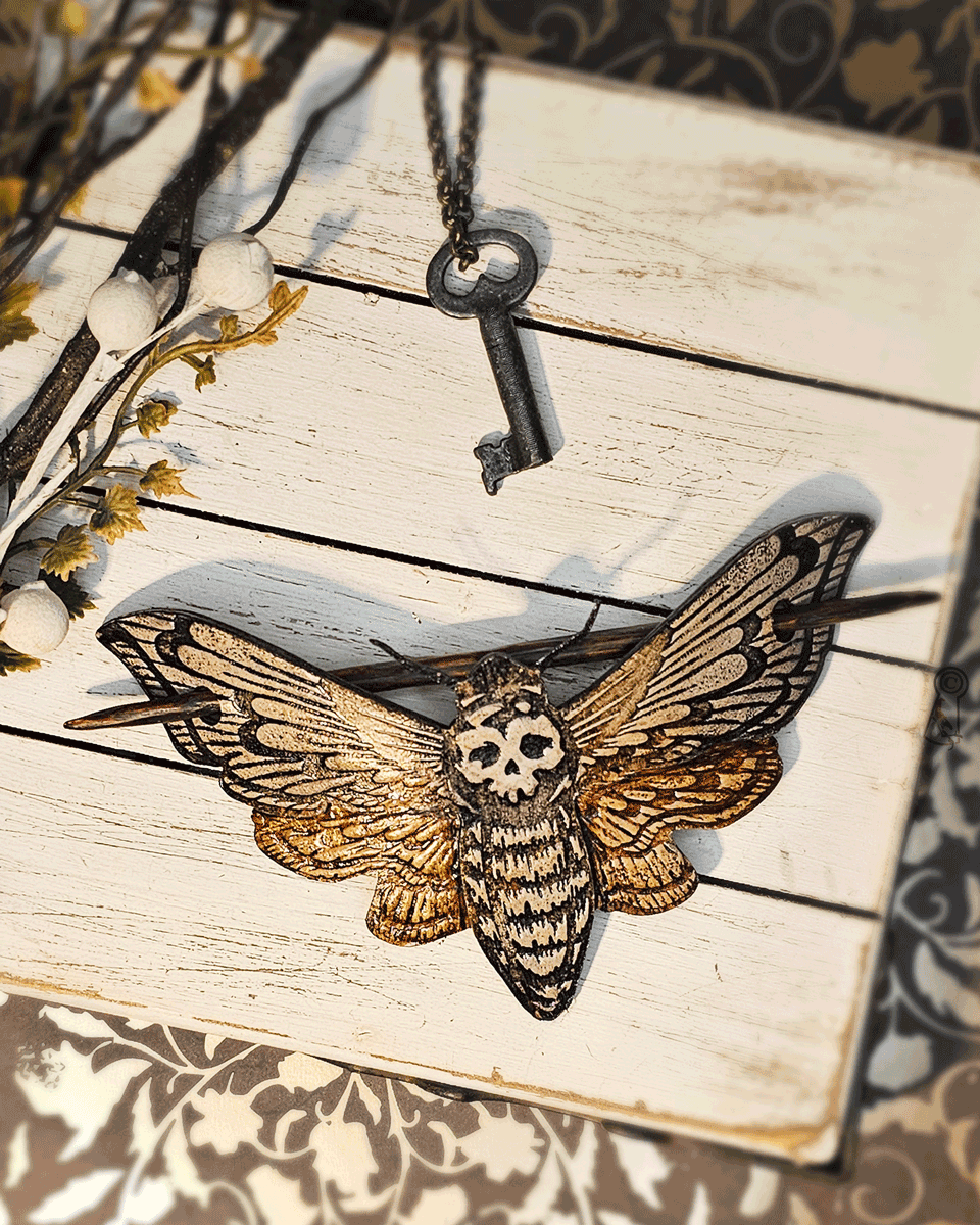 Moth-shaped hair slide with skull design placed on a wooden surface.