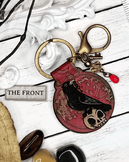 Red keychain with a crow & skull design with beads, a large clasp, and a tiny on a white surface.