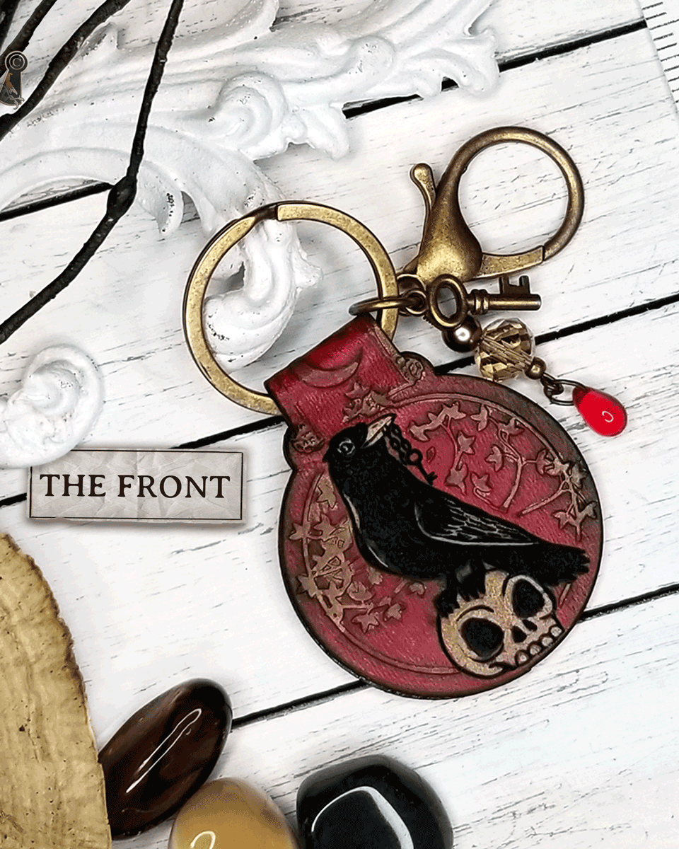 Red keychain with a crow & skull design with beads, a large clasp, and a tiny on a white surface.