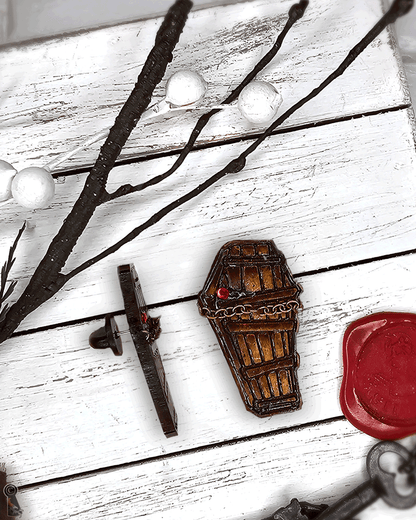 Decorative coffin charm near a key and red wax seal on a white wooden surface.