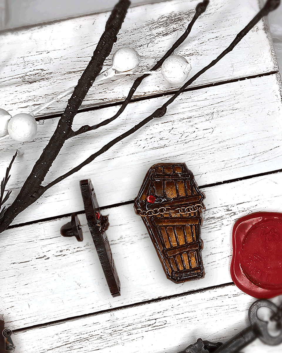 Decorative coffin charm near a key and red wax seal on a white wooden surface.