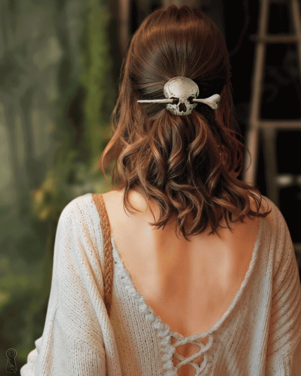 Person with leather skull and a wood, resin bone hair accessory in a wavy hairstyle, wearing a beige cardigan.