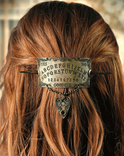 Hair accessory with Ouija board design and planchette charm on a person with long hair.