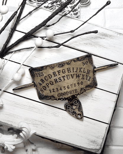 Ouija board slide together with a dark wood stick and a planchette pendant on a white wooden surface.