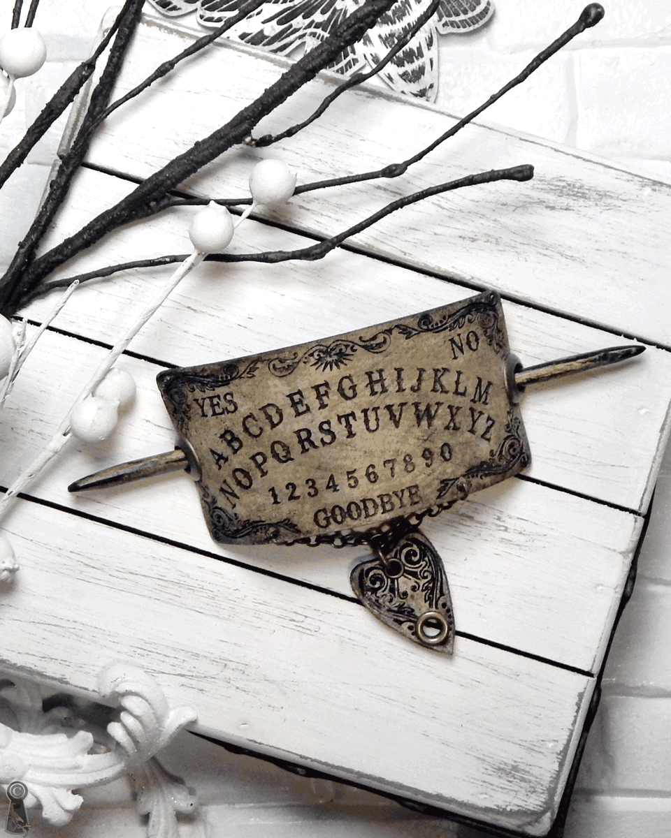 Ouija board slide together with a dark wood stick and a planchette pendant on a white wooden surface.