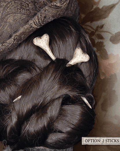 Close-up of dark styled hair with two bone hairpins, top hat, and decorative elements on a floral background.
