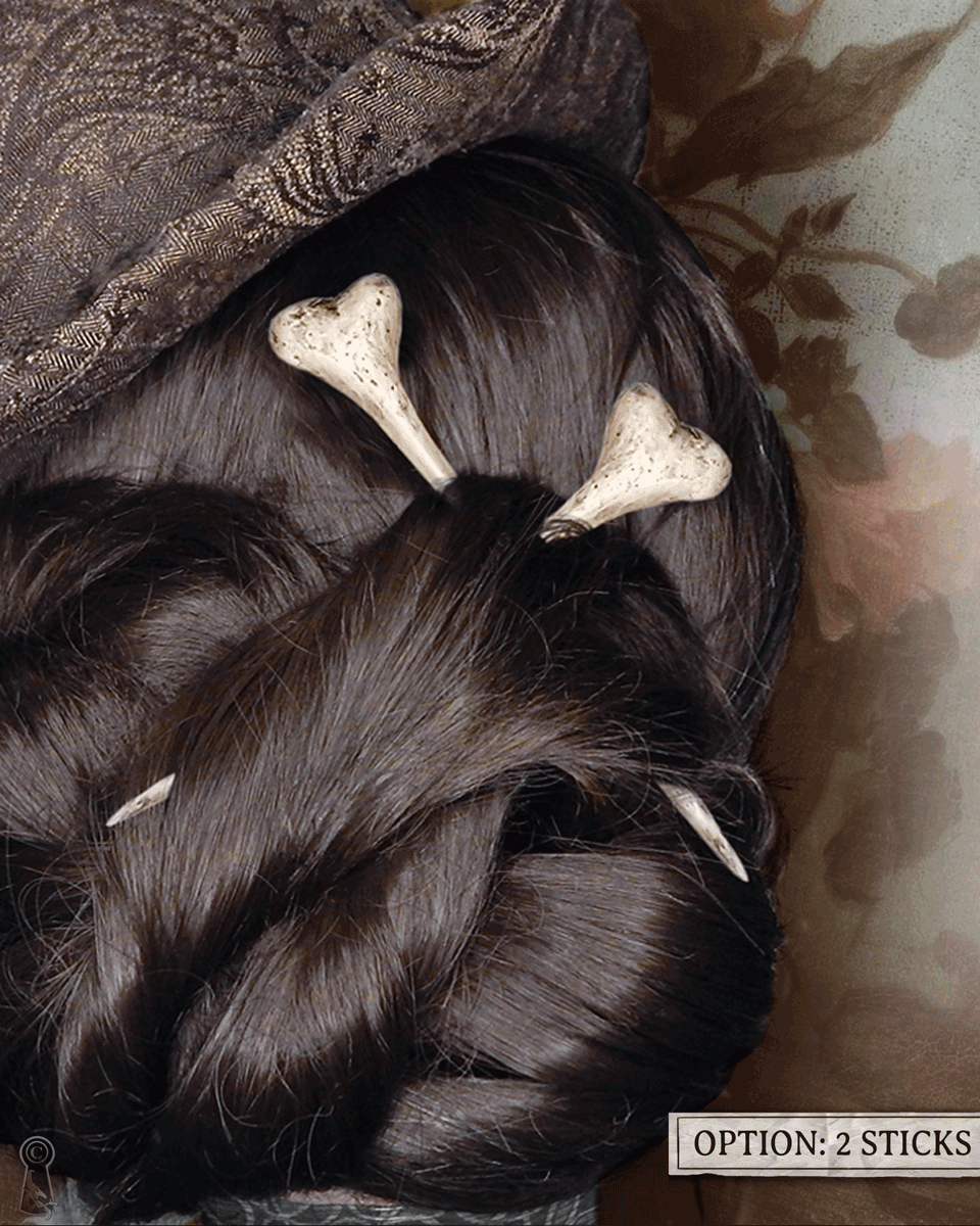 Close-up of dark styled hair with two bone hairpins, top hat, and decorative elements on a floral background.