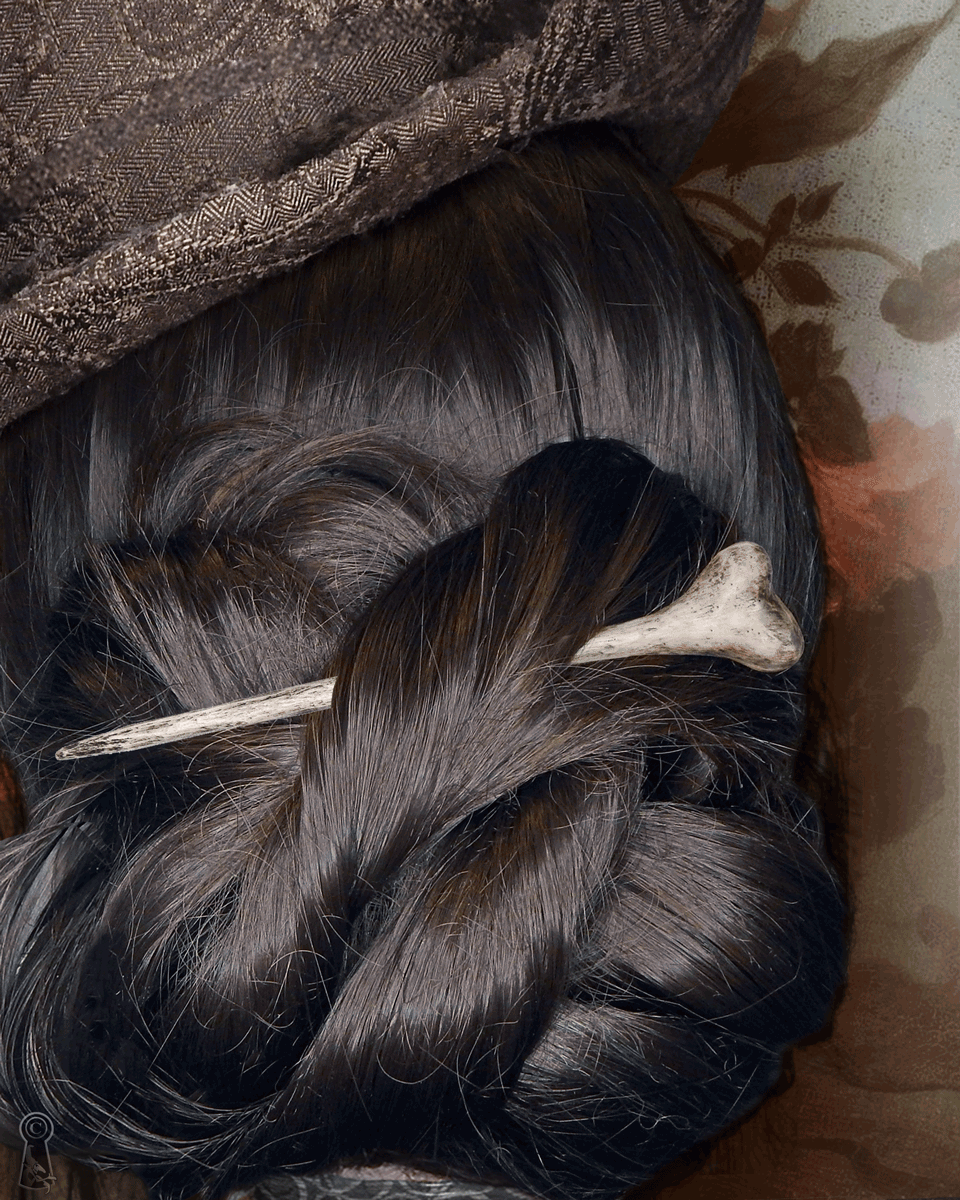 Close-up of dark styled hair with a bone hairpin, top hat, and decorative elements on a floral background.