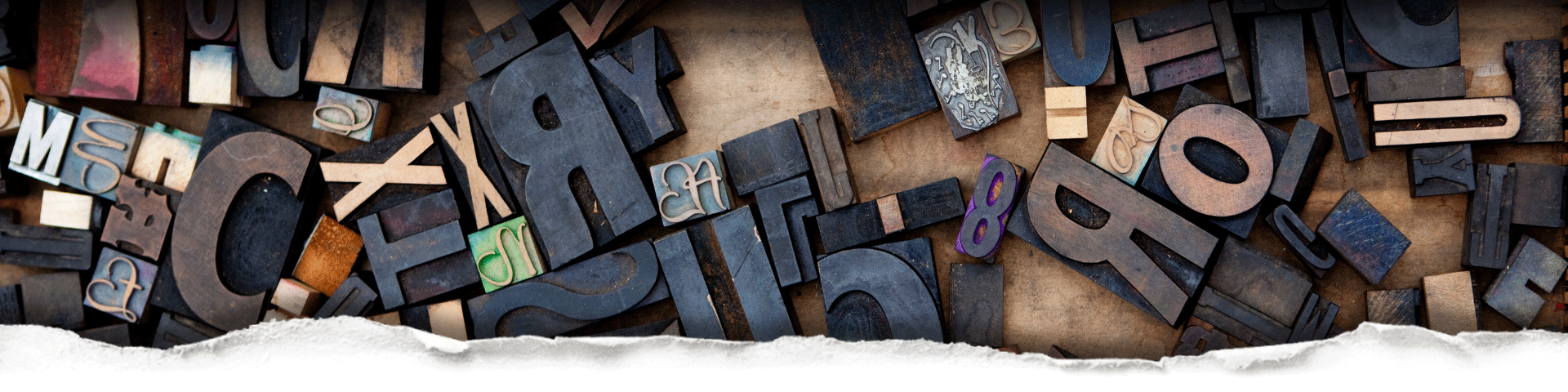Assorted wooden letter ink blocks in wood behind torn paper